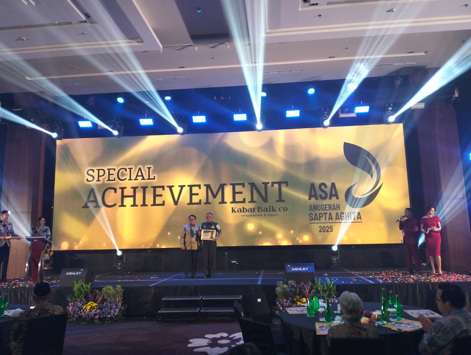 Foto : Foto : Pelda Duladi berdiri dengan bangga memegang piagam penghargaan Anugrah Sapta Aghita 2025 di atas panggung Janaloka Ballroom Surabaya