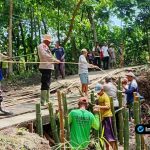 Foto : Kapolsek Modo AKP Suroso dan warga sedang bahu-membahu mengangkat batu dan mengisi karung untuk membangun tembok penahan tanah (TPT) darurat di tepi jalan yang longsor.